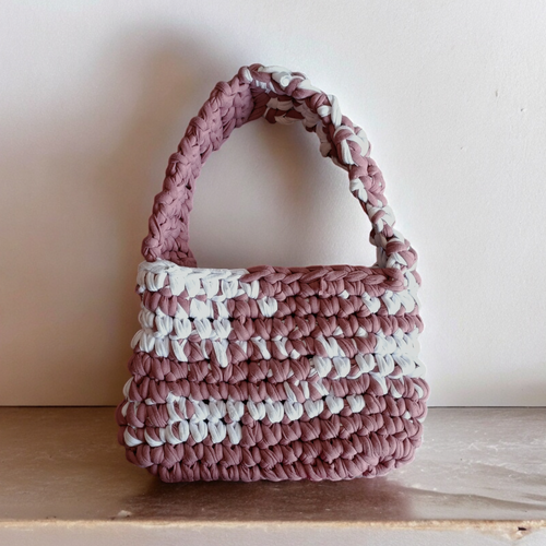 Handmade crochet bag with pink and white pattern on a wooden surface.