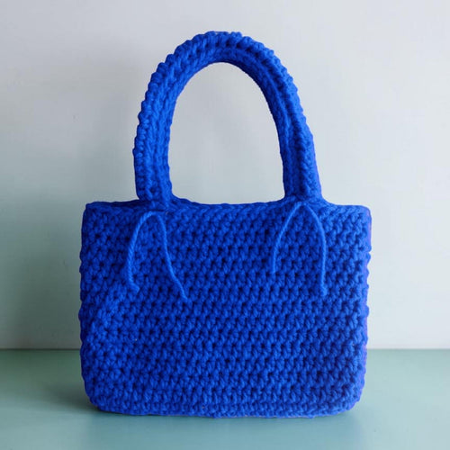 Blue crocheted handbag on a light green surface with a light grey background