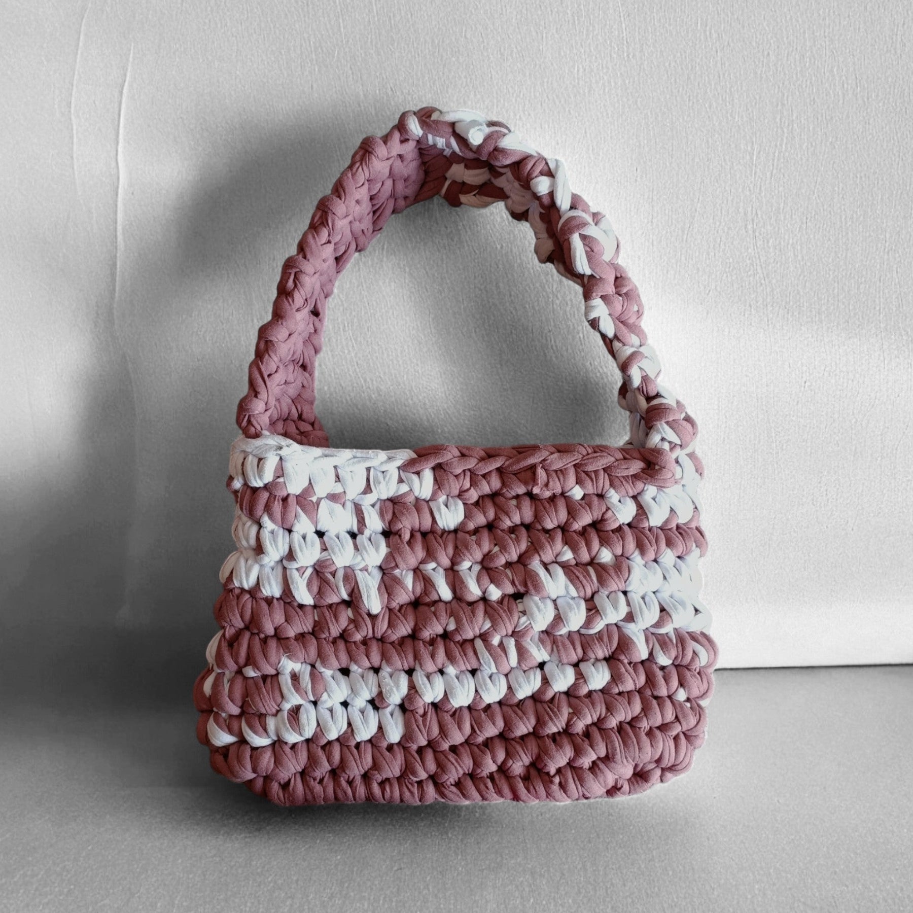 Pink and white crochet handbag on a light grey background